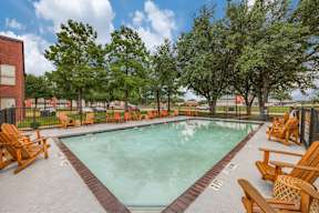 A pool surrounded by wooden chairs and trees.