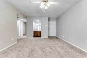 A spacious room with a carpeted floor and a ceiling fan.