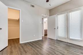 A room with white walls and wooden flooring, featuring a door with a fan above it.