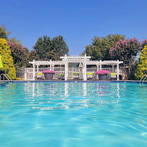 A pool with a white fence and pink flowers in the background.