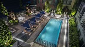 A swimming pool surrounded by lounge chairs and umbrellas at night.
