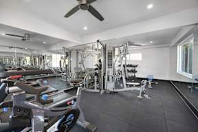 A spacious gym with a variety of equipment including treadmills, weights, and a ceiling fan.