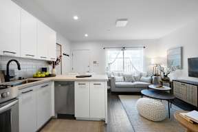 A modern kitchen with white cabinets and a grey sofa.