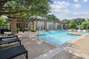 A pool surrounded by a patio with a black bench.