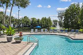 A pool with a fountain in the background and chairs around it.