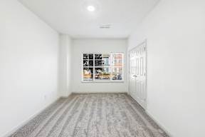 A room with a striped carpet and a window showing a view of a street.