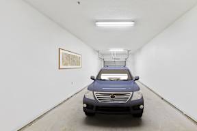 A blue car is parked in a white room with a painting on the wall.