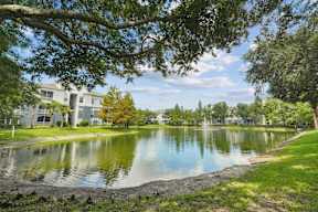 A serene lake surrounded by trees and buildings under a clear sky.