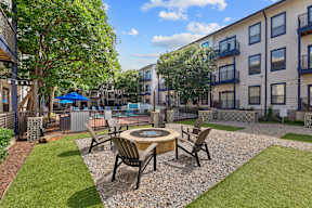 A patio with a table and chairs is surrounded by grass and trees.