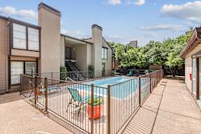 A pool surrounded by a fence with a chair and a potted plant.