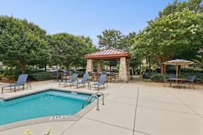 A pool area with a gazebo and lounge chairs.