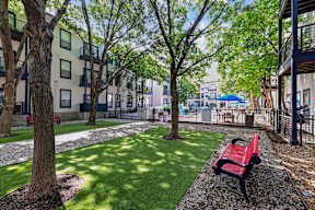 A red bench sits on a gravel path in a grassy courtyard.