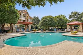 A large swimming pool surrounded by trees and chairs.
