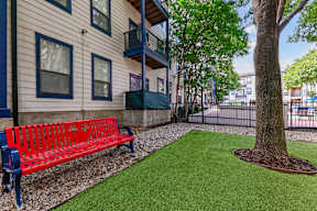 A red bench sits on a gravel path in front of a building.
