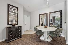 A room with a white table and chairs and a black dresser with a mirror above it.