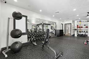 A gym with a variety of equipment including dumbbells, weight plates, and a bench press.