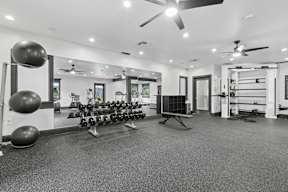 A spacious gym with a variety of equipment including dumbbells, weight plates, and a bench press.