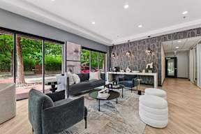 A modern living room with a grey sofa, a black coffee table, a grey armchair, a white pouf, and a grey rug.