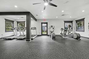 A spacious gym with treadmills, elliptical machines, and a fan.