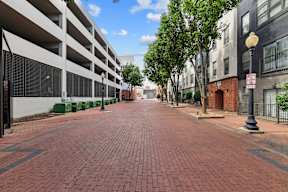A long brick road with a parking garage on the left and a building on the right.