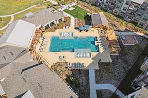 A large swimming pool surrounded by a wooden deck and lounge chairs.