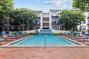 A pool surrounded by chairs and trees in front of a building.
