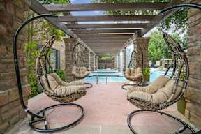 A patio with a pool and hanging chairs.