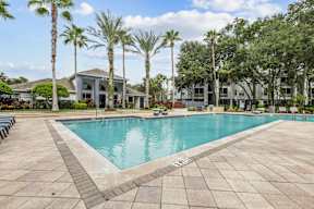 A swimming pool surrounded by palm trees and a building in the background.