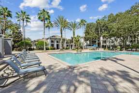 A pool surrounded by palm trees and lounge chairs.