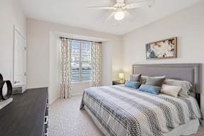 A bedroom with a bed, a ceiling fan, and a window with curtains.