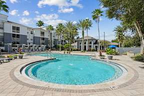 A swimming pool surrounded by palm trees and a building in the background.