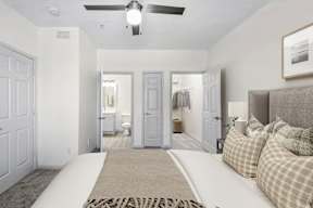 A bedroom with a bed, pillows, and a rug in the foreground with a hallway and bathroom visible in the background.
