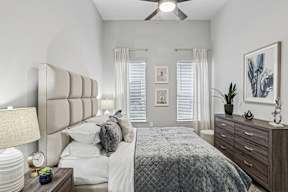 A bedroom with a large bed, a nightstand with a lamp, and a ceiling fan.