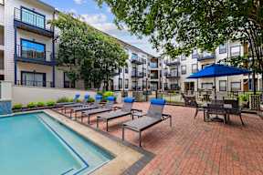 A pool surrounded by chairs and umbrellas in a courtyard.