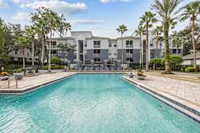 A swimming pool in front of a building surrounded by palm trees.