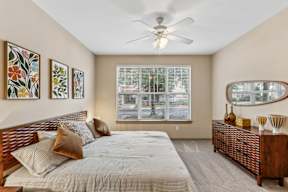 A bedroom with a bed, a dresser, and a window with blinds.