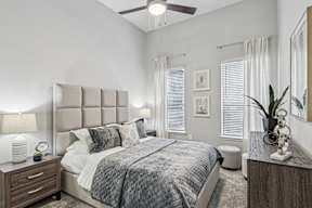 A bedroom with a large bed, a ceiling fan, and a nightstand with a lamp.