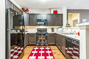 A kitchen with dark wood cabinets and a red and white rug on the floor.