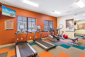 A gym with orange walls and a variety of equipment including treadmills and exercise bikes.