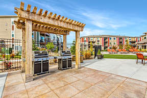 A wooden pergola is in front of two grills and a fence.