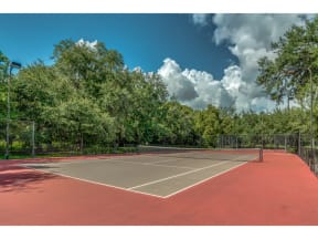 a tennis court with trees and a blue sky with clouds