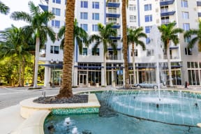 a fountain in front of a building with palm trees