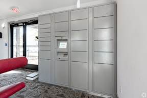 A grey metal locker room with a red bench and a door with a window.
