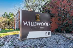 A sign for Wildwood Apartment Homes is displayed in front of a brick building.