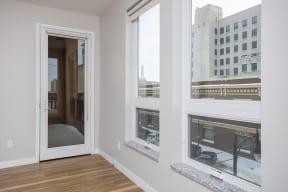 a bedroom with three large windows and a door that leads to a balcony  at RoCo Apartments, Fargo, 58102