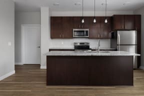 a kitchen with a large island with granite countertops and dark wood cabinets  at RoCo Apartments, North Dakota, 58102