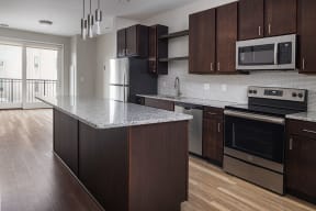 a kitchen with dark wood cabinets and an island with a granite countertop and stainless steel appliances  at RoCo Apartments, Fargo, 58102