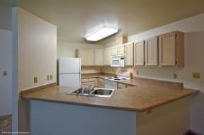 Kitchen here at Brighton Park with wooden cabinets, a white fridge, a stove, and a microwave. A large countertop with a sink extends into the room.