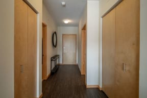 Hallway here at Gallery Flats Apartment Homes with wooden floors and doors, white walls, recessed lighting, a round mirror on the wall, and a slim black console table, creating a minimalist and inviting atmosphere.
