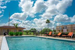 Outdoor swimming pool with lounge chairs and palm trees at Los Cedros Apartments